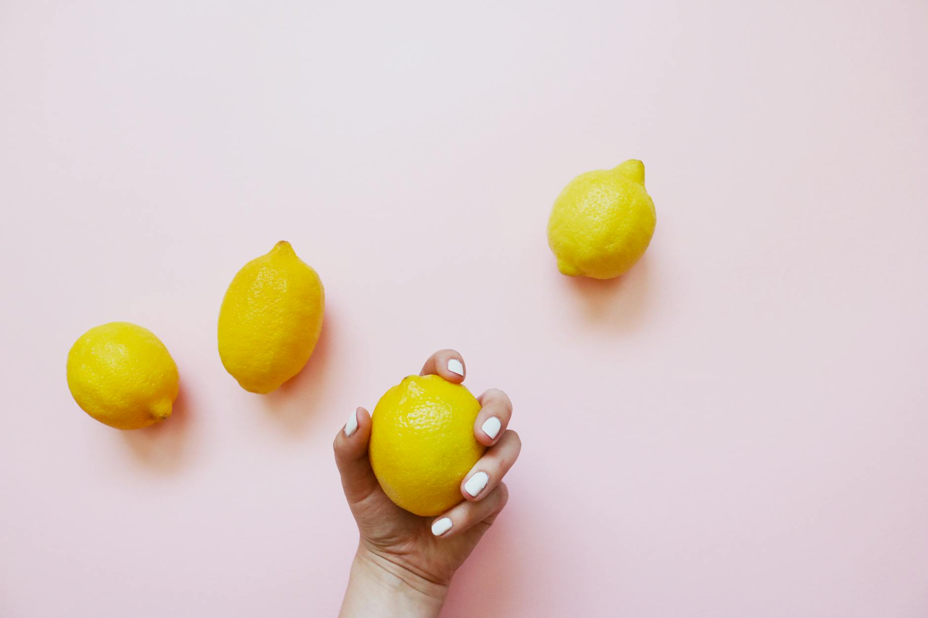 Hand holding a lemon on soft pink background, representing sensitive clitoral care with Hallo Nancy Lemons products