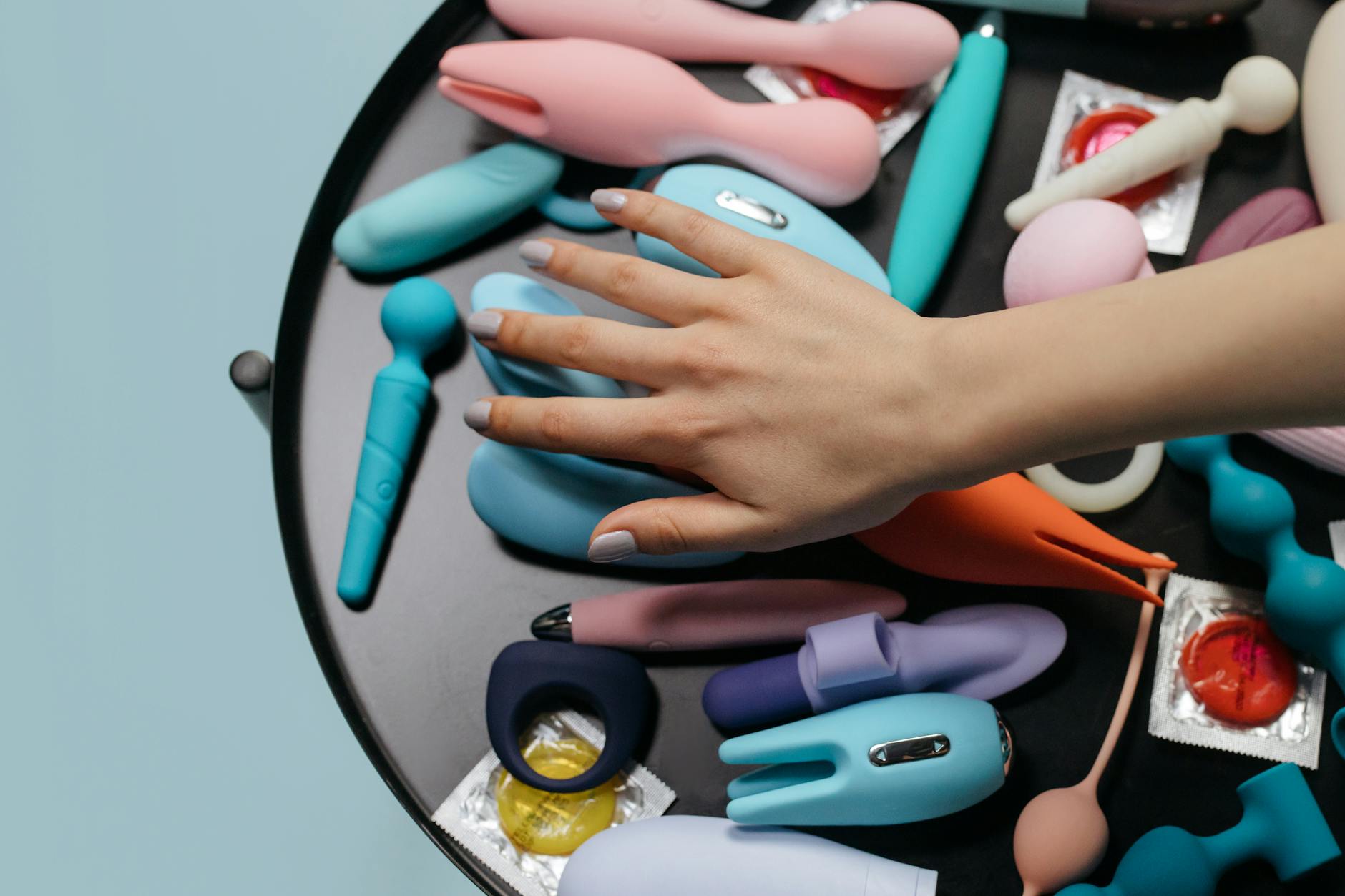 Woman holding blue and pink silicone clitoral vibrators in a thoughtful moment