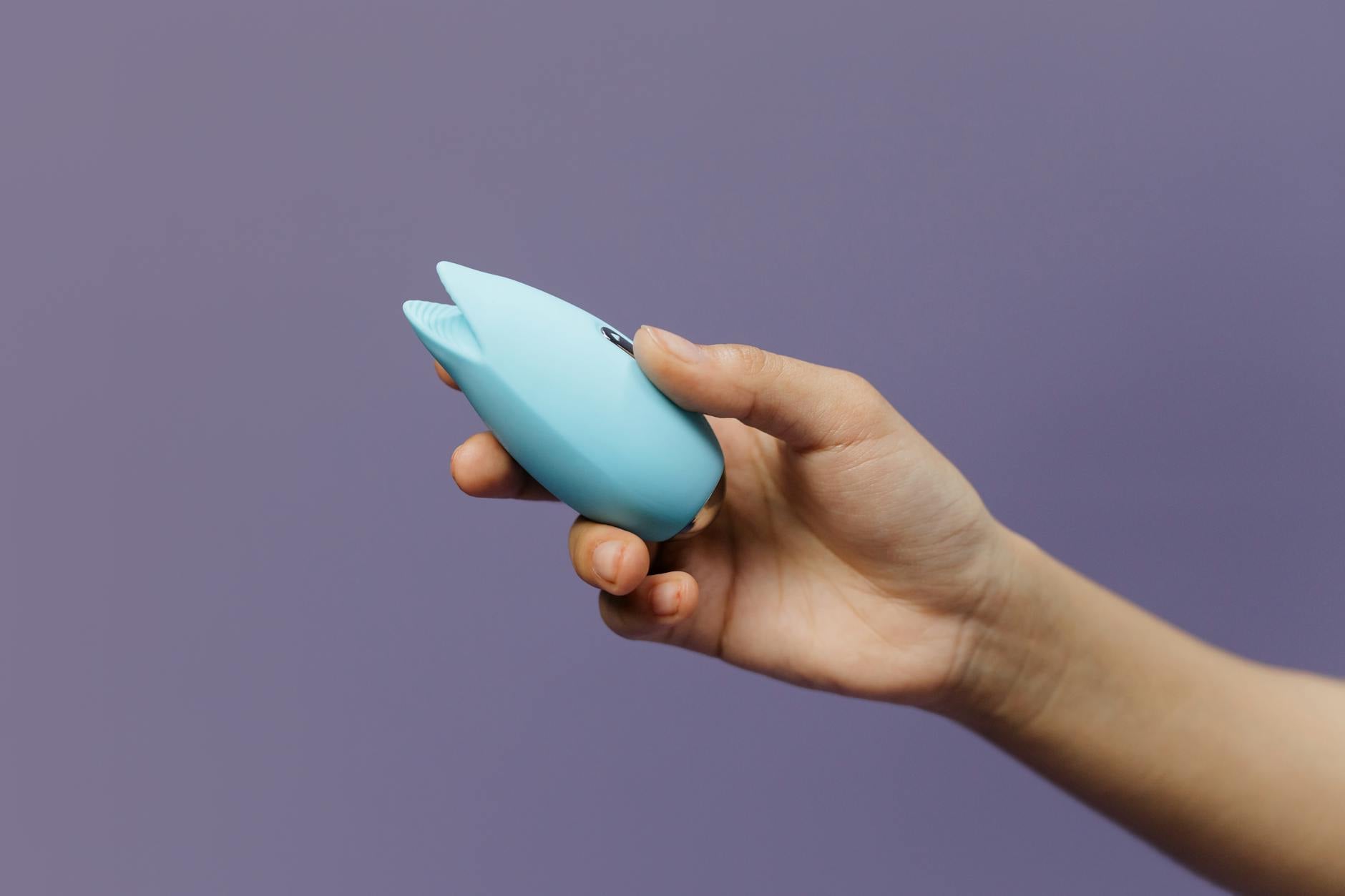 A silicone clitoral vibrator held in hand against a purple background, showing color and tactile design