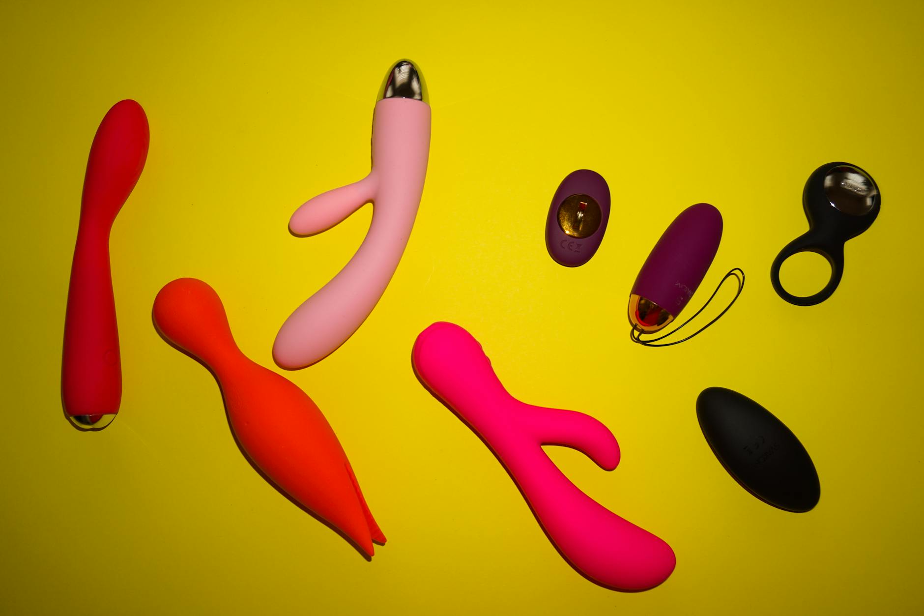 Vibrant collection of modern adult toys displayed on bright yellow surface, showcasing design diversity